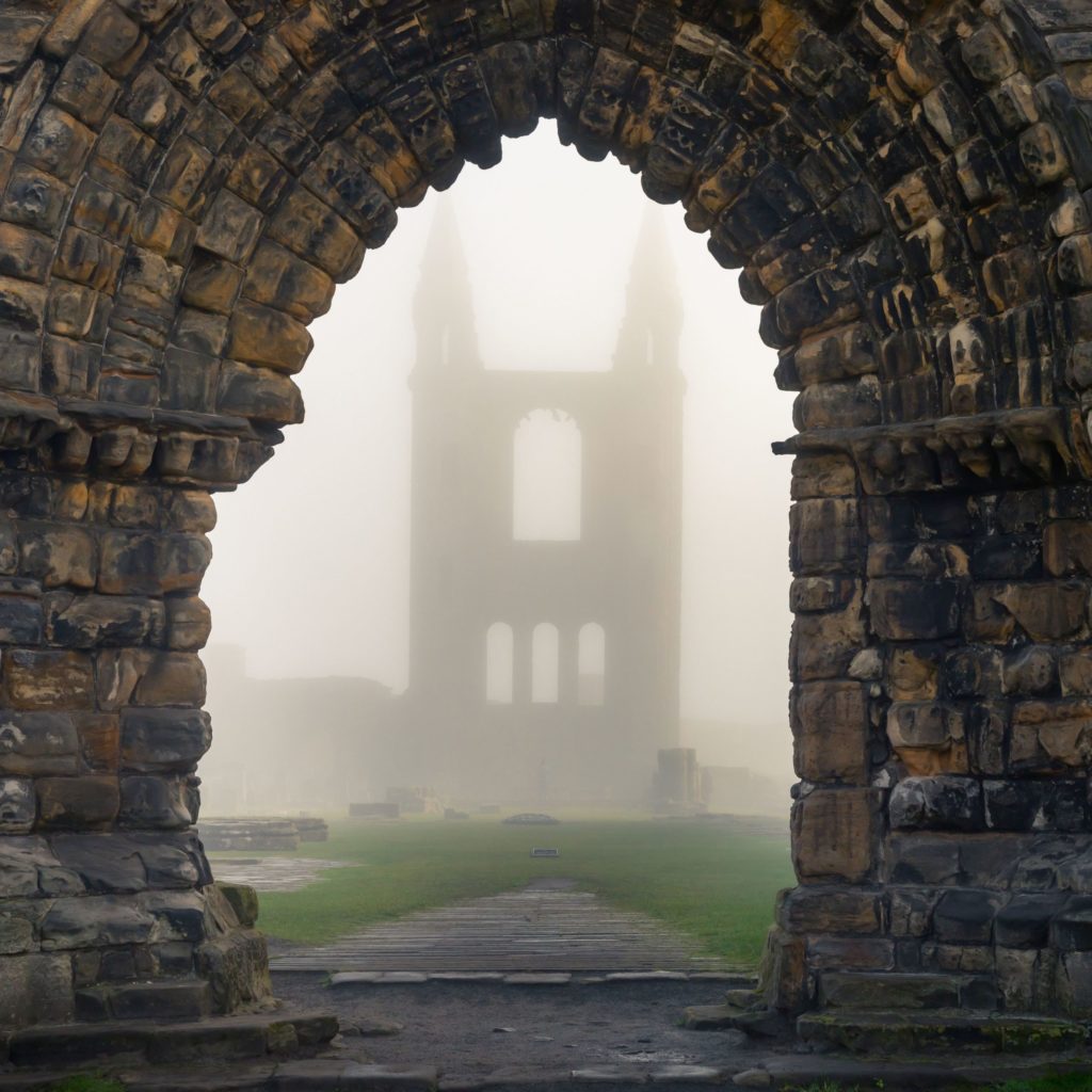 A misty archway with a ruined building beyond it.