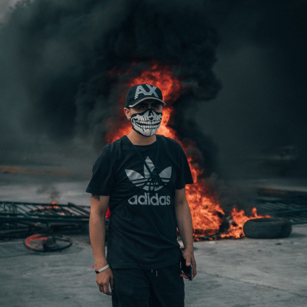 A man in a mask standing in front of a tire fire