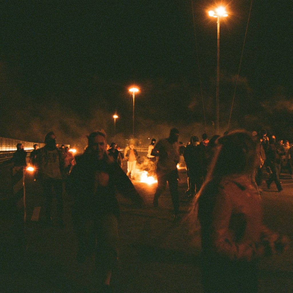 People walking past a fire in the darkness